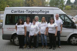 Gruppenbild Mitarbeiterinnen und Mitarbeiter der Tagespflege in Braunfels vor dem weissen Bus der Caritas, mit dem die Gäste der Tagespflege abgeholt und nach Hause gebracht werden.