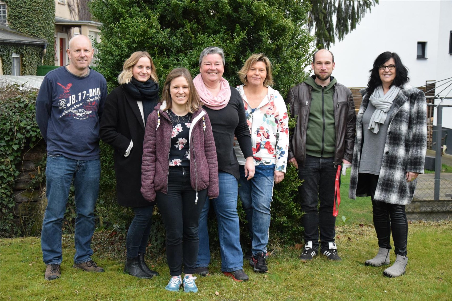 Sieben Mitglieder des Teams (2 Maenner und 5 Frauen) stehen im Garten und schauen in die Kamera. 